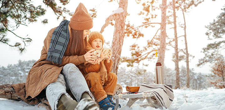 Mutter und Kind sitzen mit heißem Tee im Schnee